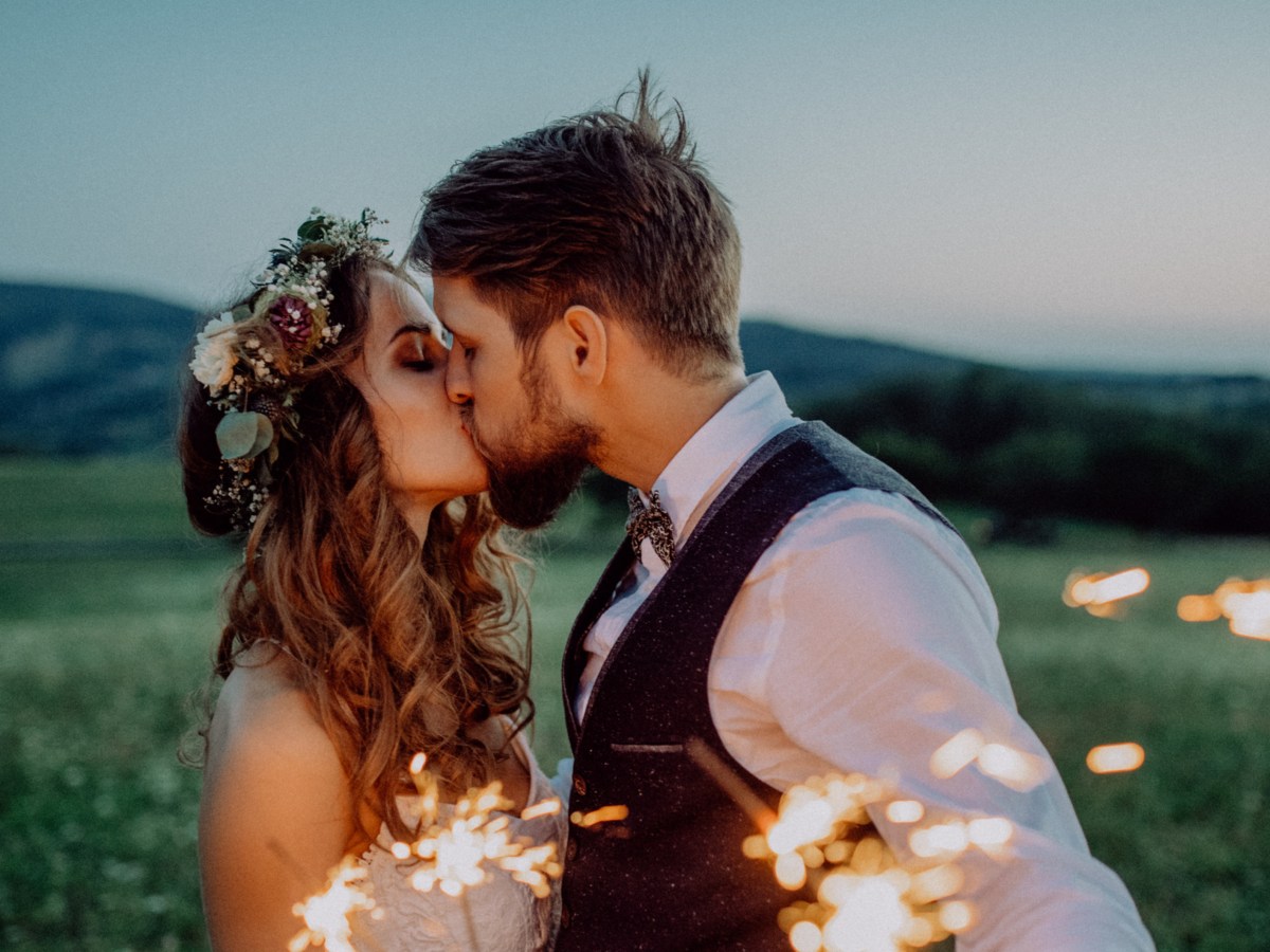 Hochzeitspaar, das sich auf Wiese mit Wunderkerzen küsst