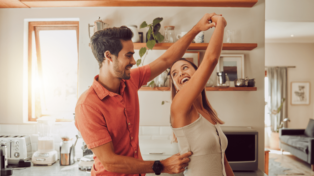 Mann und Frau in der Küche, die glücklich am Tanzen sind und lachen.