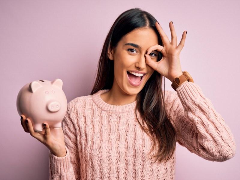 Frau vor lila Hintergrund mit Sparschwein in der Hand