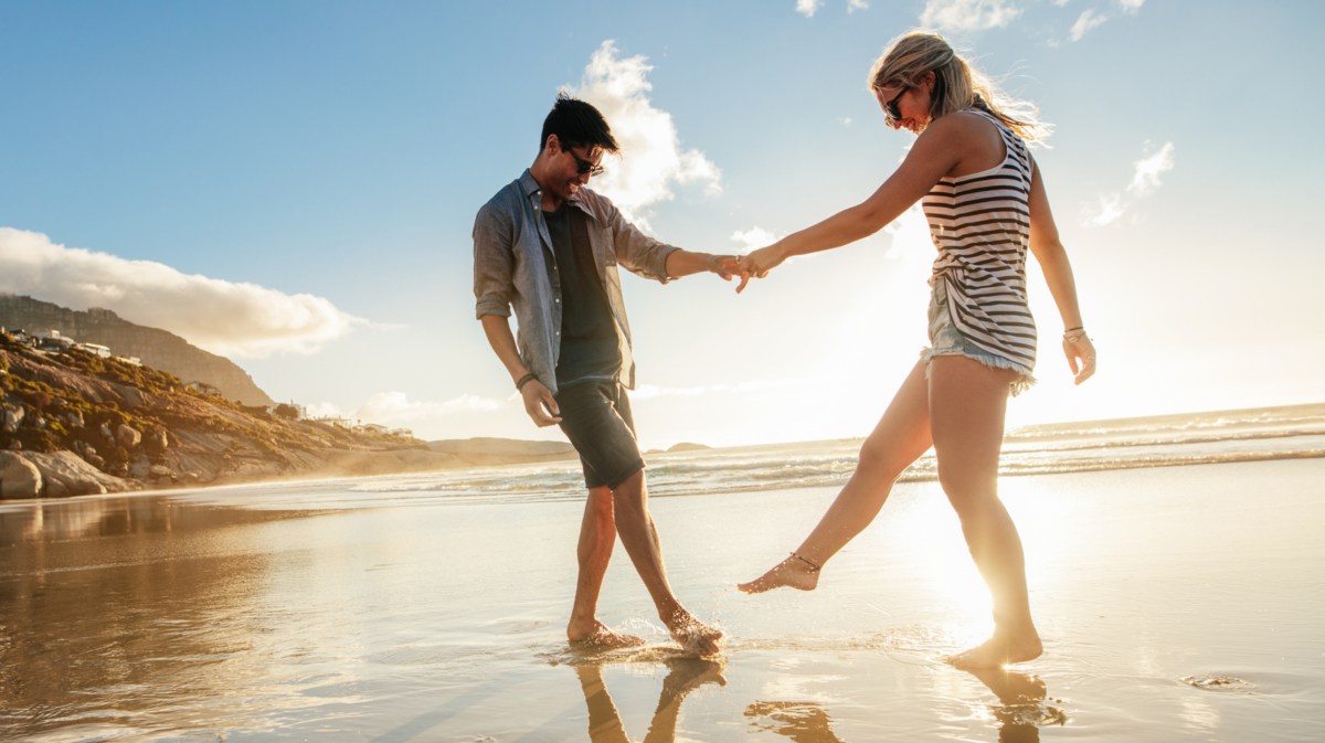 Pärchen am Strand hält sich an den Händen und tanzt