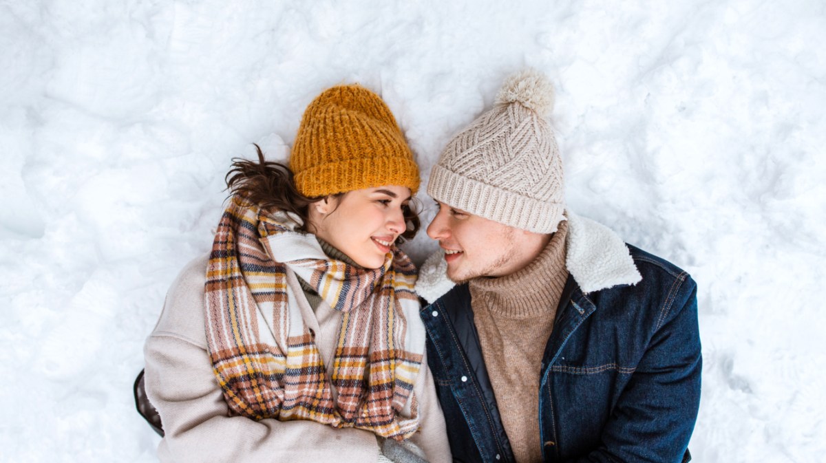 Pärchen, das gemeinsam im Schnee liegt und sich anlächelt