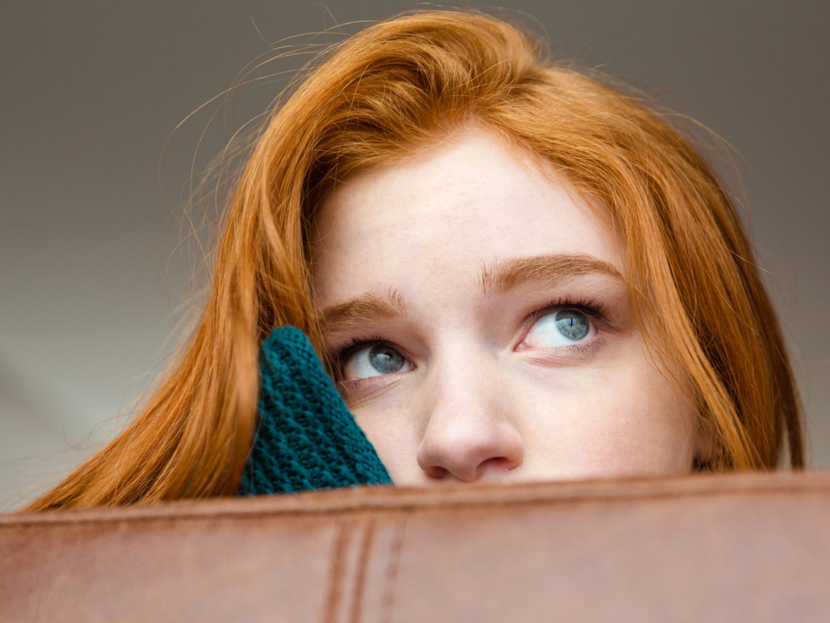 Frau auf Sofa, die nachdenklich in die Ferne guckt