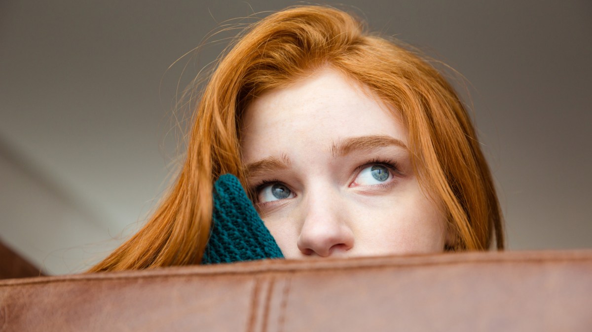 Frau auf Sofa, die nachdenklich in die Ferne guckt