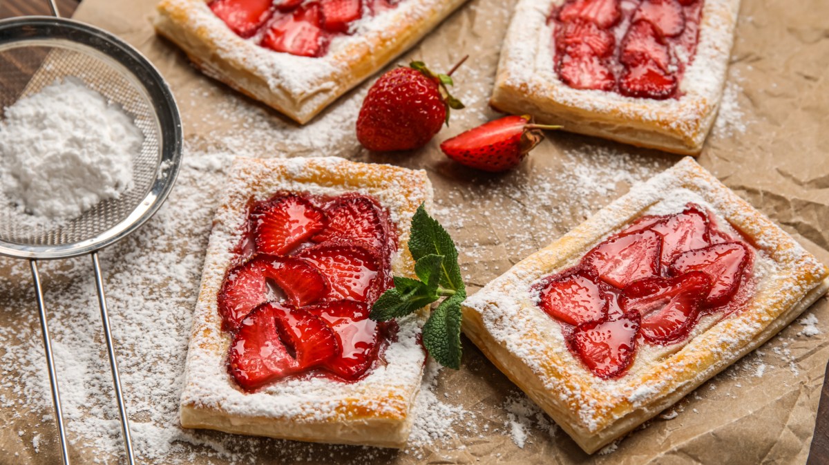 Blätterteig-Teilchen mit Erdbeeren und Puderzucker auf Backpapier.