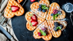 Herzwaffeln mit Früchten auf dunklem Teller.
