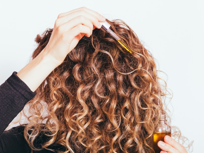 Frau mit Locken wendet Haaröl an