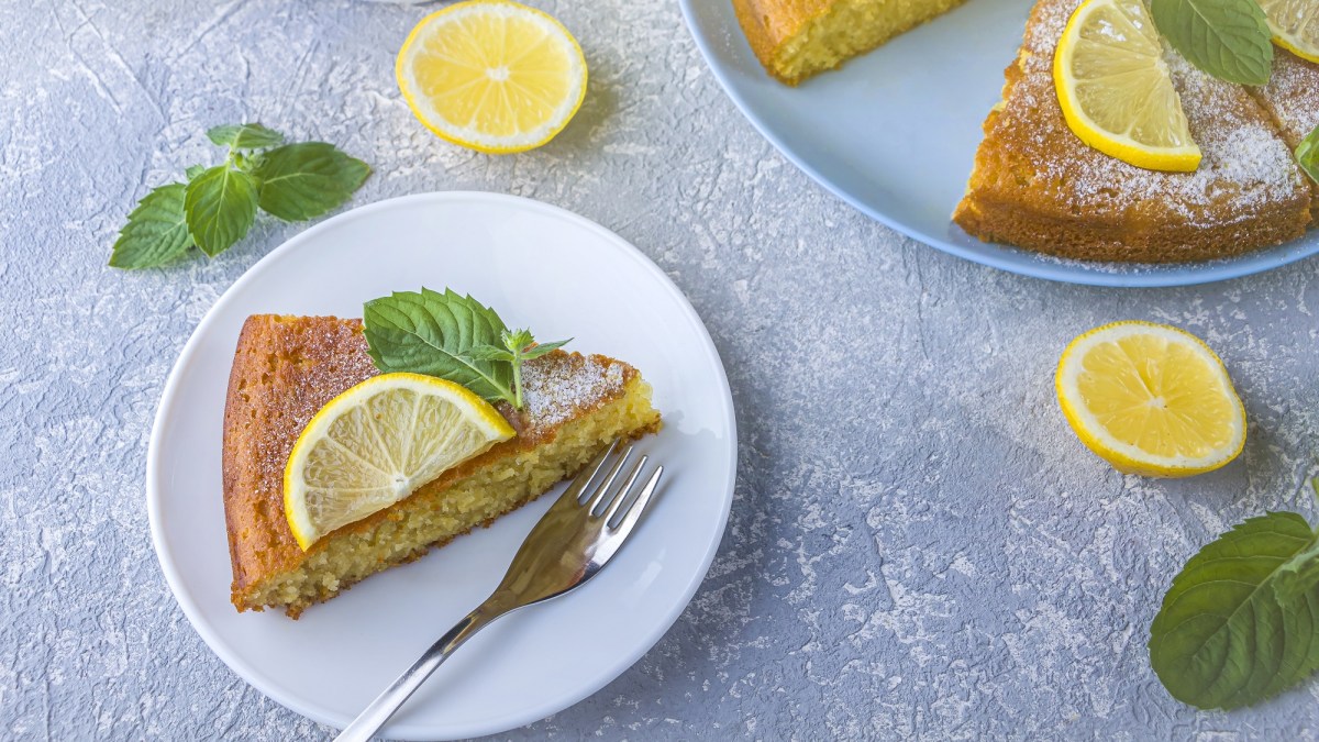 Draufsicht: ein angeschnittener Zitronen-Grießkuchen. Einige Kuchenstücke liegen auf zwei blauen Tellern verteilt. Die Kuchen sind mit Zitronenscheiben und Minzblättern garniert.