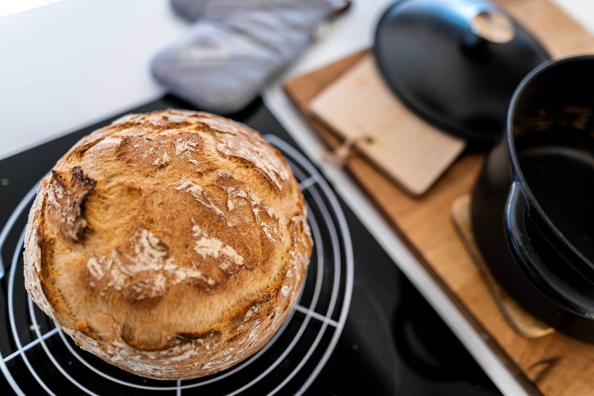 Brotlaib kühlt auf einem Küchenrost ab, daneben steht noch der Topf, in dem es im Ofen gebacken wurde.