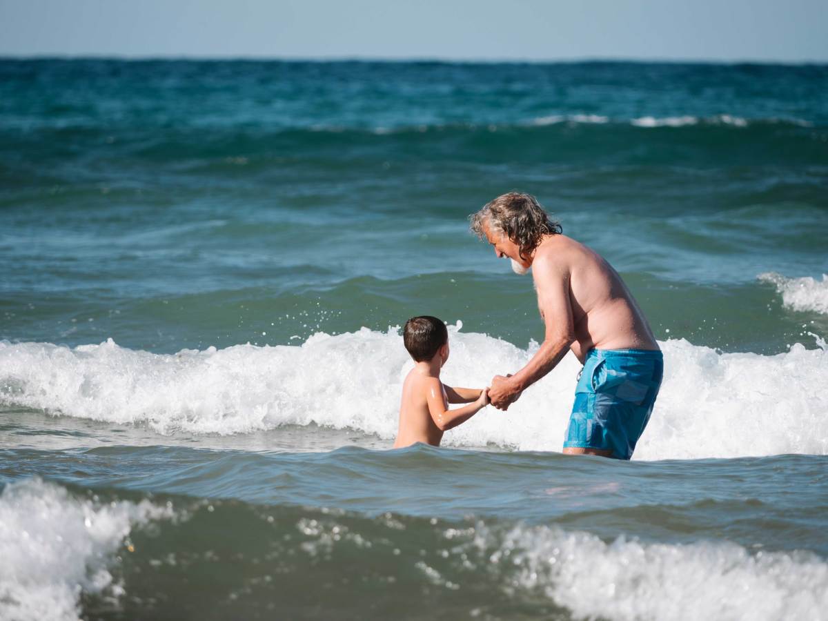 Großvater und Enkel spielen im Meer und springen zusammen über Wellen.