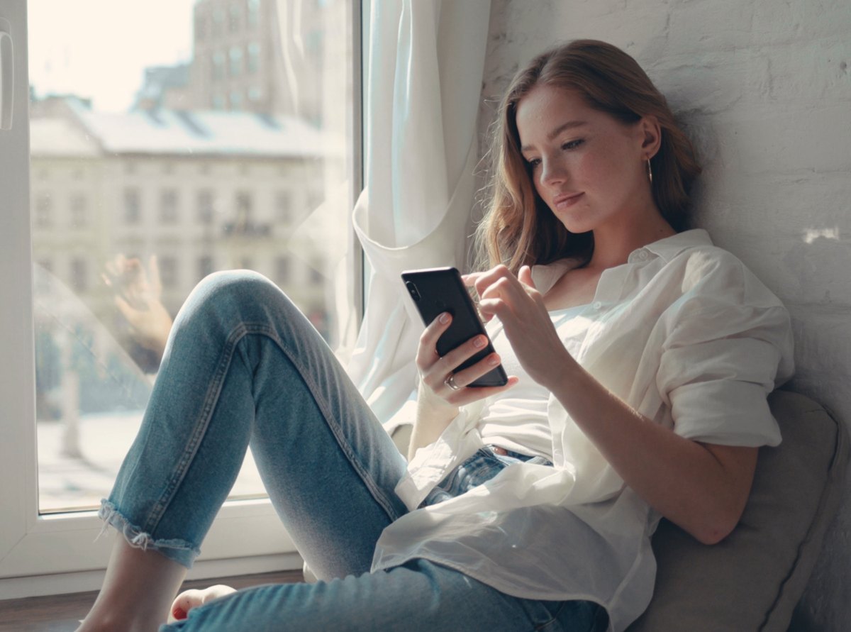 Close up hübsche junge Frau sitzt auf einer Fensterbank zu Hause und Texting auf ihrem Telefon Kommunikation weiblich suchen Nachricht Handy