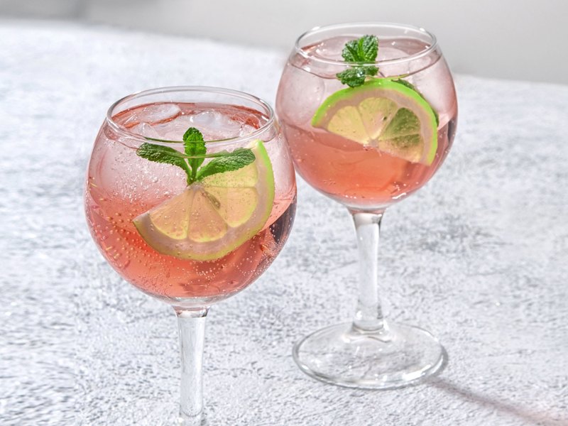 Sarti Spritz: Hellrosa Getränk in Weingläsern mit Limettenscheiben