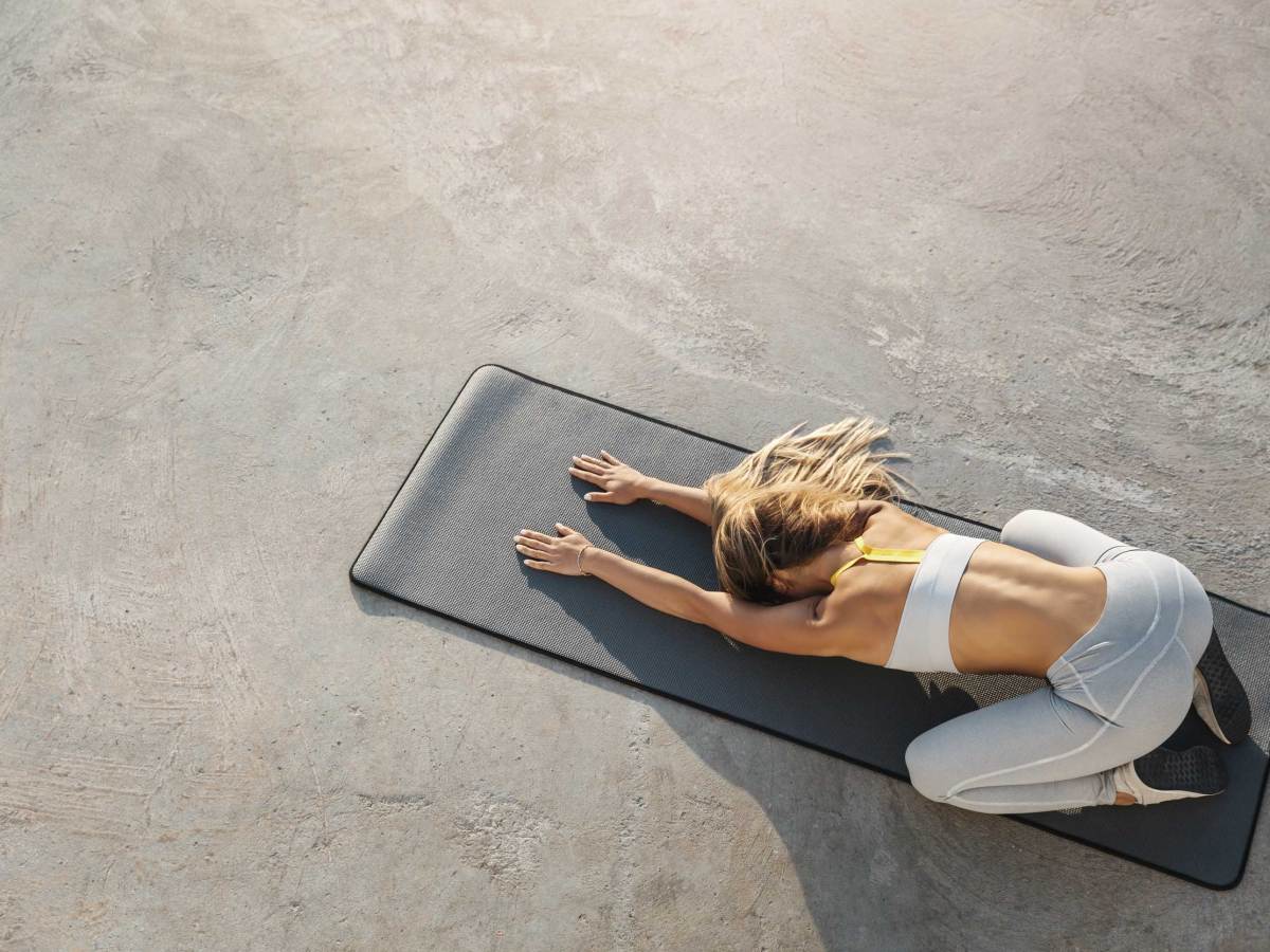 Attraktive, sportliche Frau, die auf einer Yogamatte sitzt und Balasana, die Kinderhaltung, dehnt, trainiert, Asana-Posen w&auml;hrend des morgendlichen Trainings macht, die H&auml;nde nach vorne ausstreckt