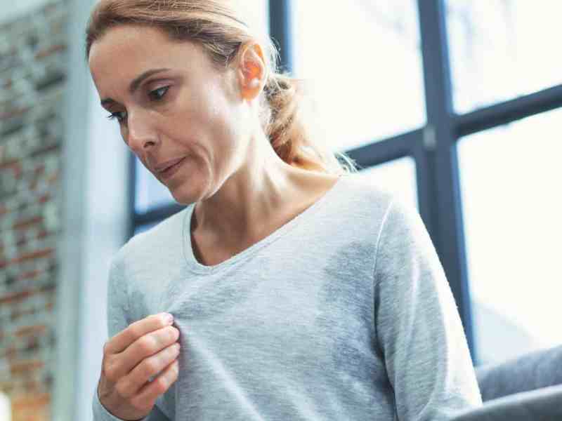 Frau schwitzt in ihrem Shirt stark und versucht es auszulüften.