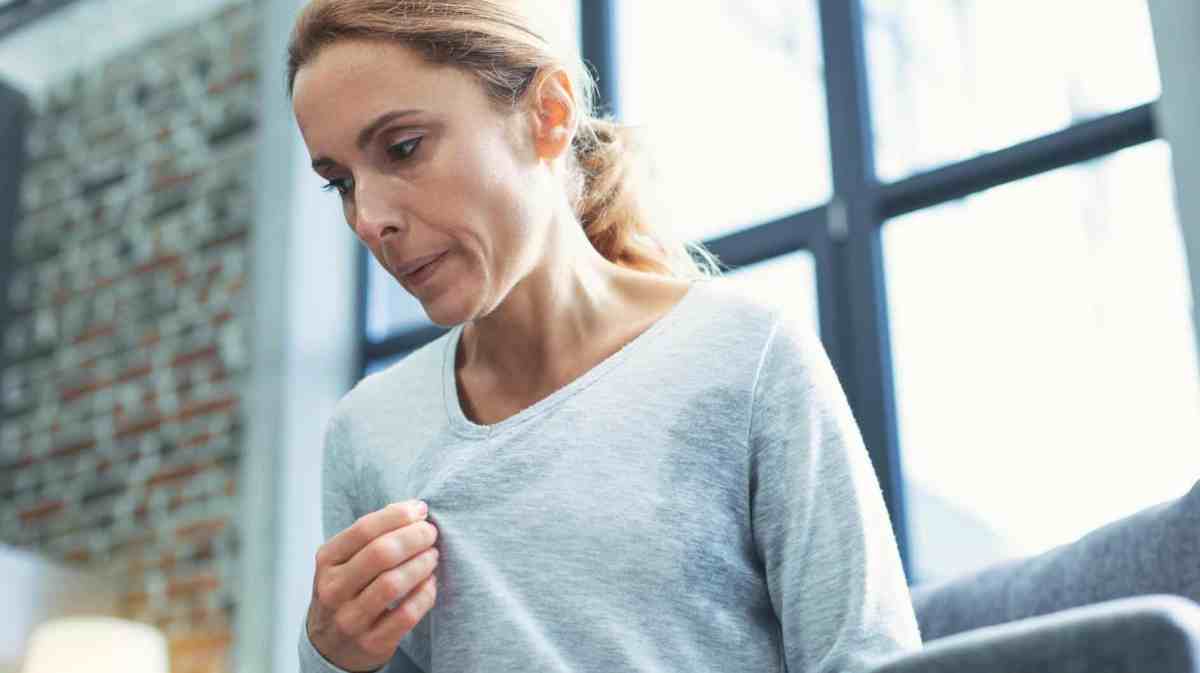 Frau schwitzt in ihrem Shirt stark und versucht es auszulüften.