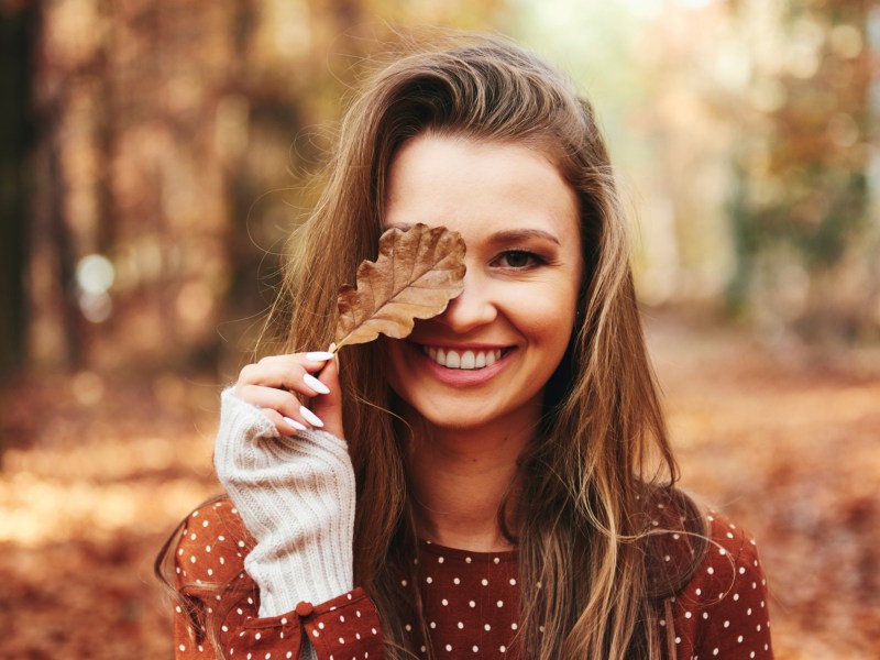 Frau hält Herbstblatt vor Gesicht.