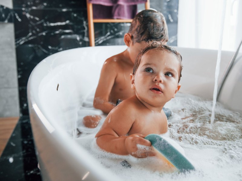 Geschwister sitzen in der Badewanne mit Schaum und Spielzeug.