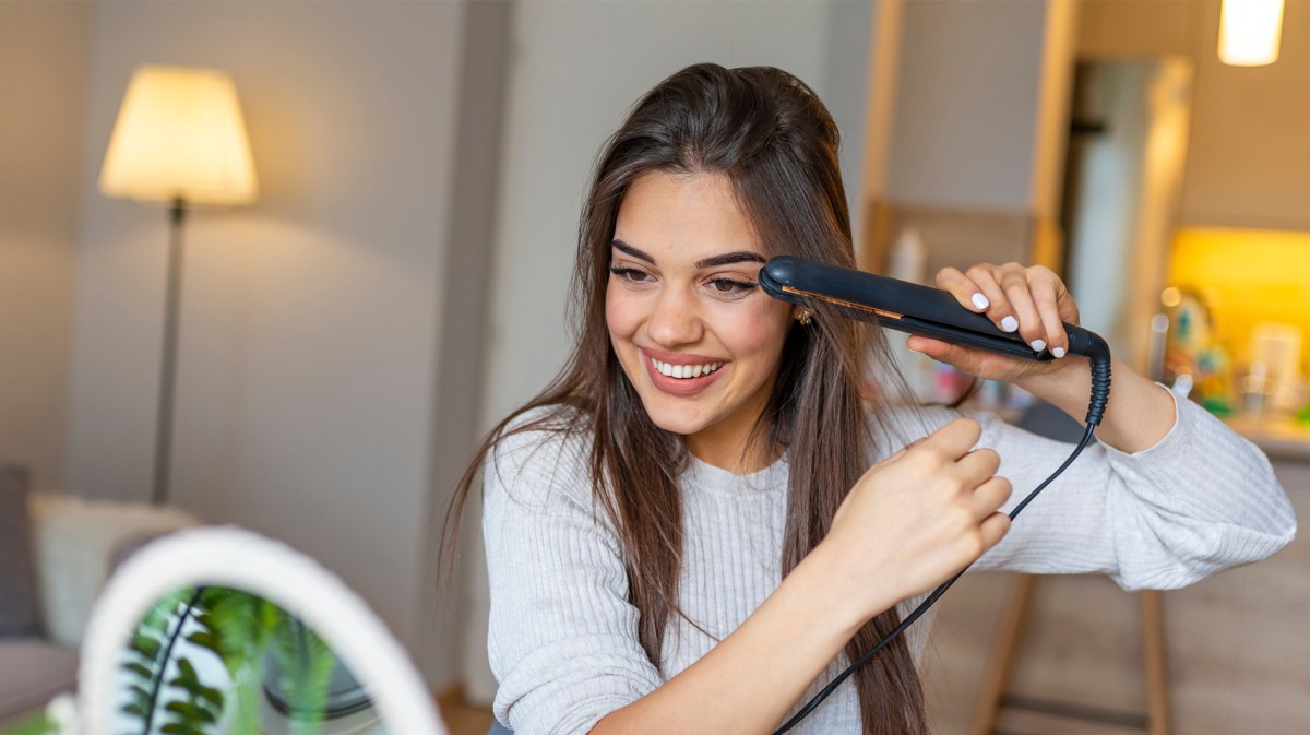 Frau beim Glätten ihrer langen Haare.