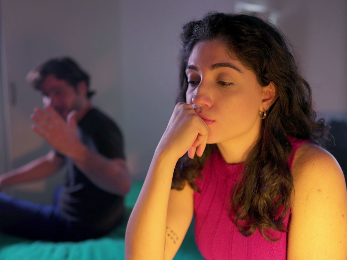 Frau im Vordergrund schaut unglücklich drein. Im Hintergrund wütender Mann