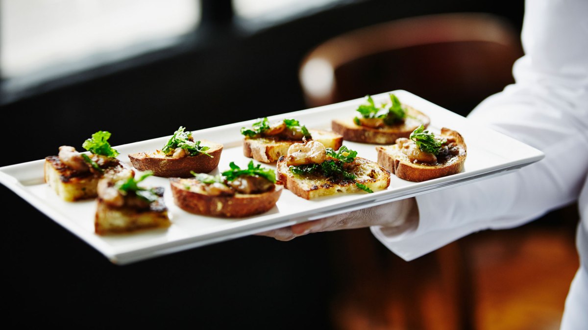 Eine Hand hält ein Tablett mit Häppchen.