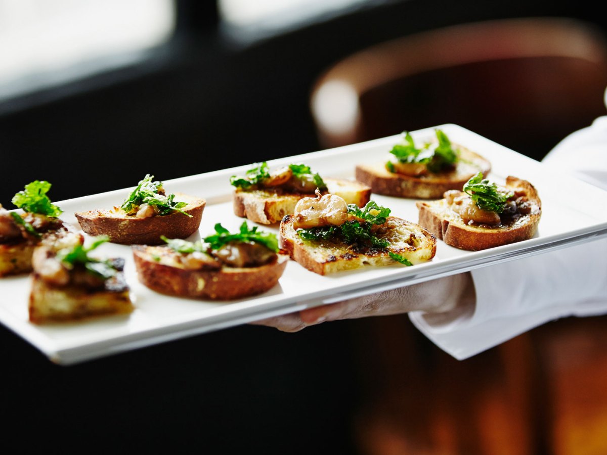 Eine Hand hält ein Tablett mit Häppchen.