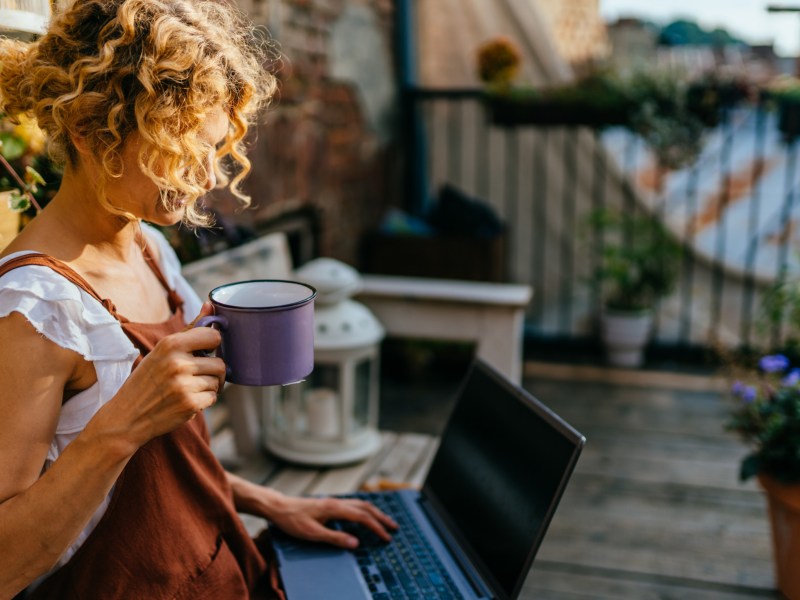 Frau sitzt mit einem Laptop auf dem Balkon und macht Home Office im Freien