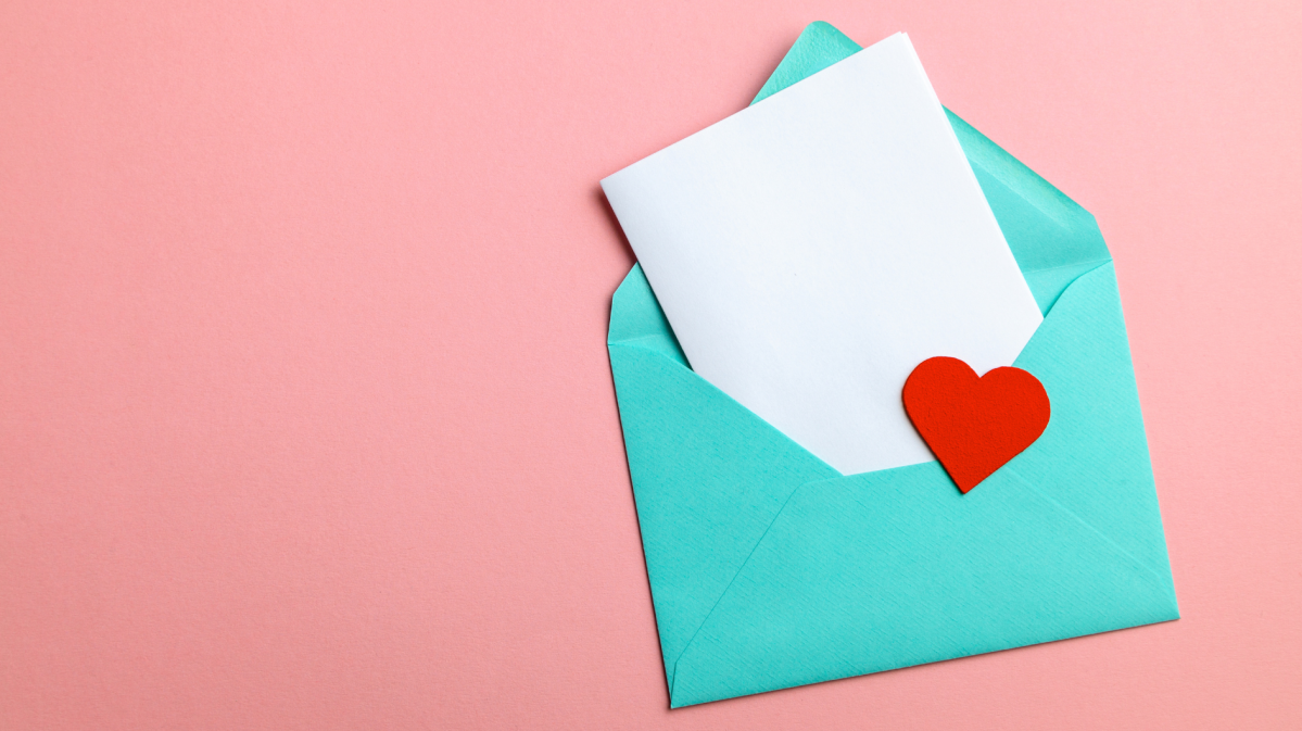 Geöffneter türkisfarbener Umschlag mit weißem Papier und einem roten Herz auf zartem rosafarbenem Untergrund.
