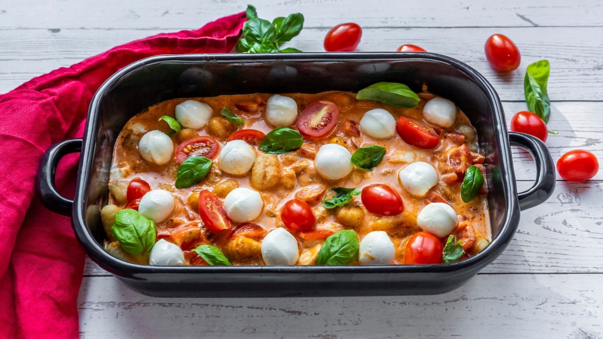 Ofen Gnocchi mit Tomate und Mozzarella in schwarzer Auflaufform auf weißem Holz.