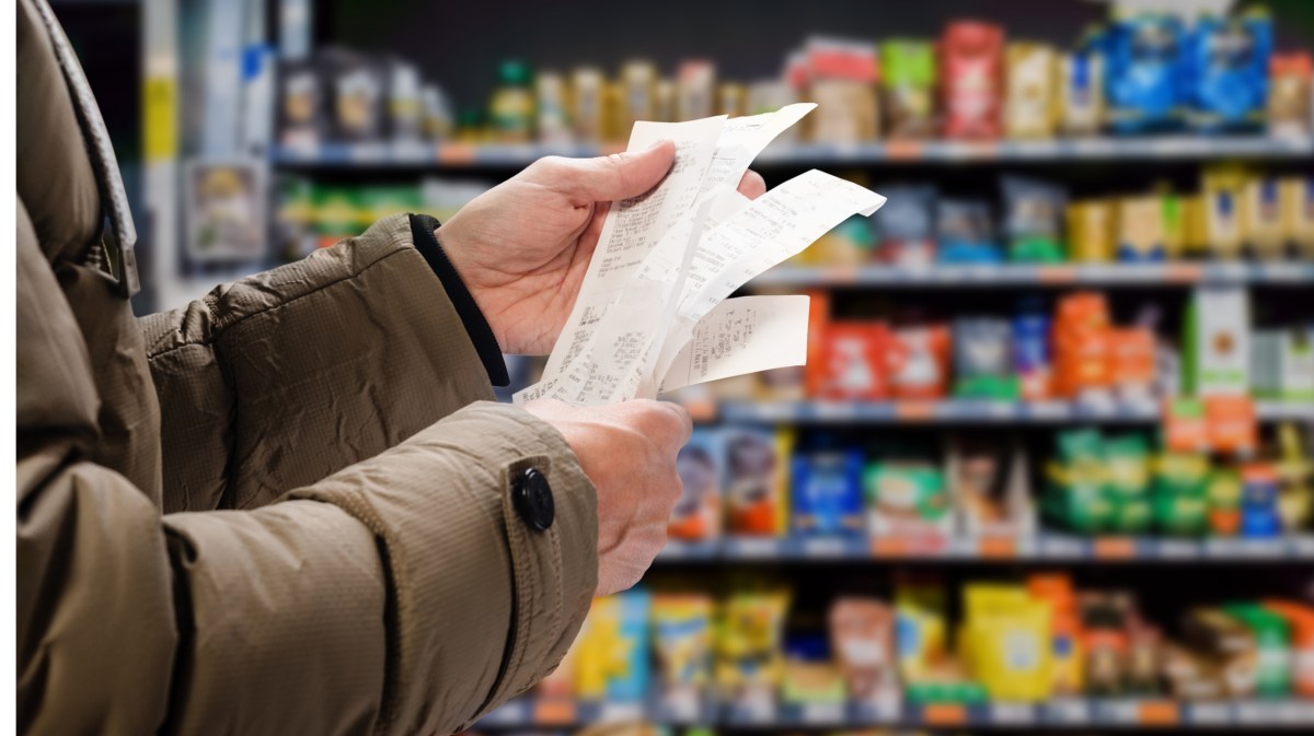 Arme eines Mannes, der im Supermarkt drei Kassenzettel liest und vergleicht