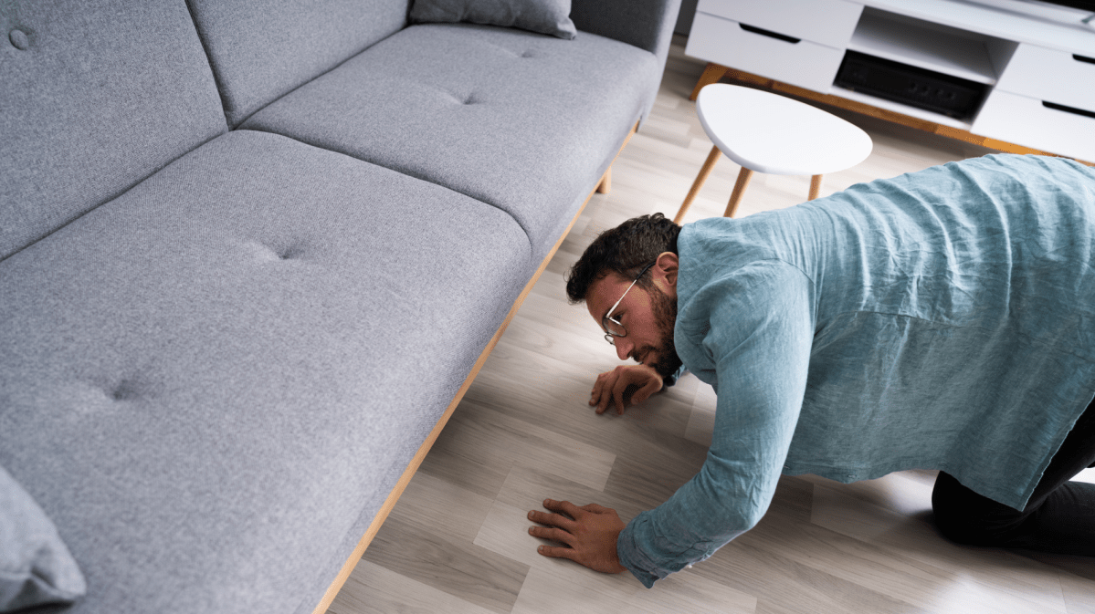 Junger Mann kniet auf dem Boden und sucht unter dem Sofa etwas