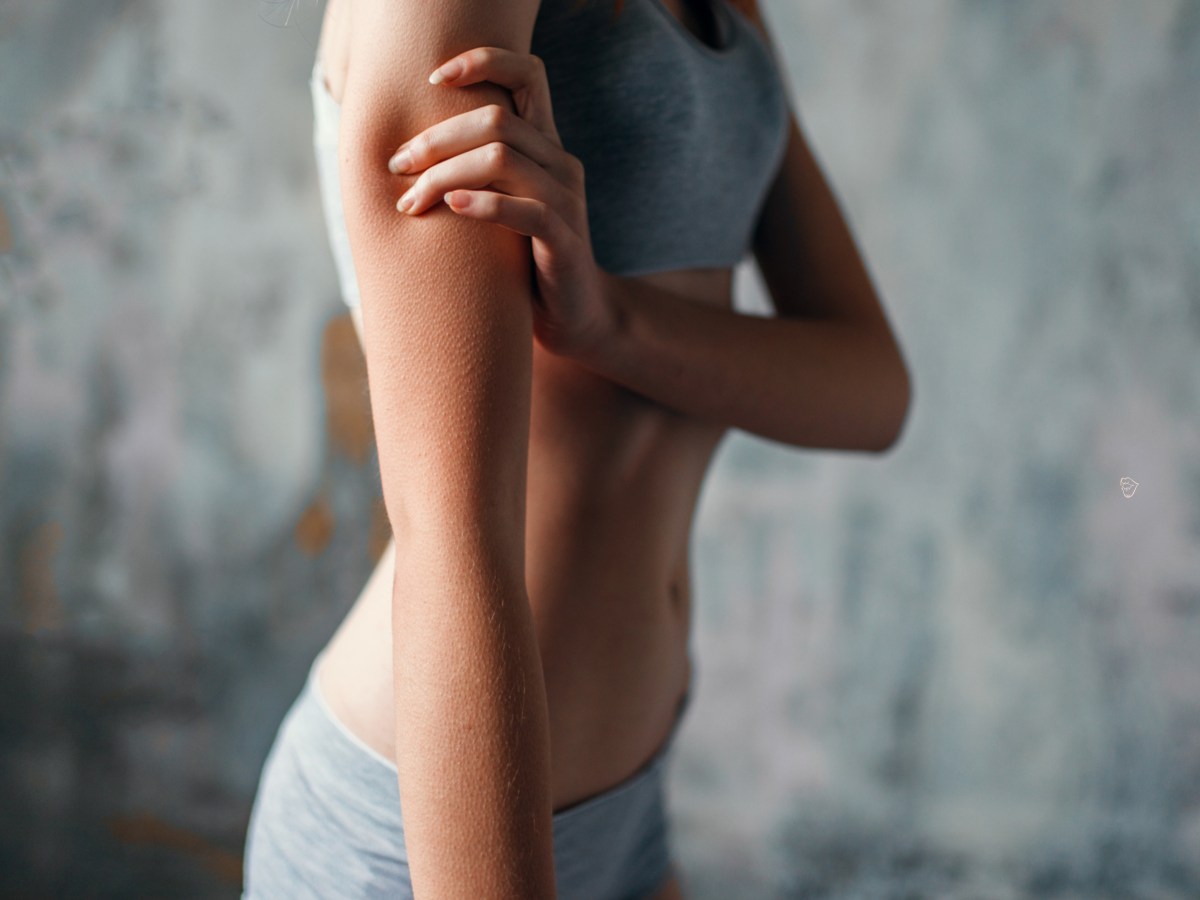 D&uuml;nne Frau in grauer Unterw&auml;sche, die sich an den Oberarm packt