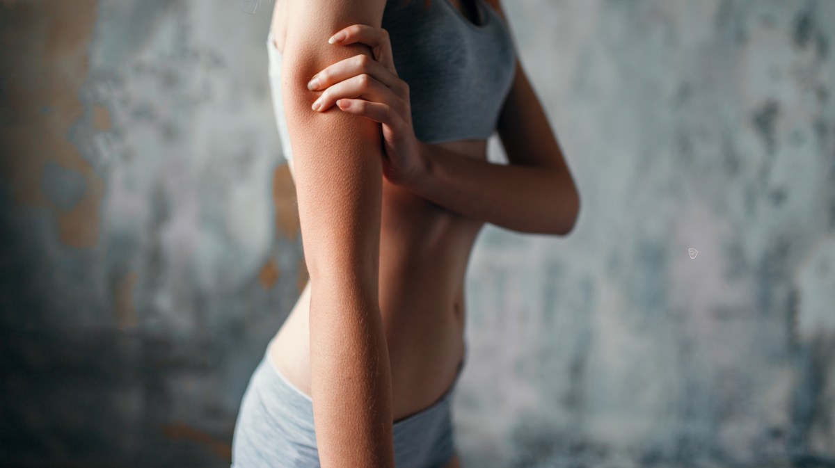 Dünne Frau in grauer Unterwäsche, die sich an den Oberarm packt