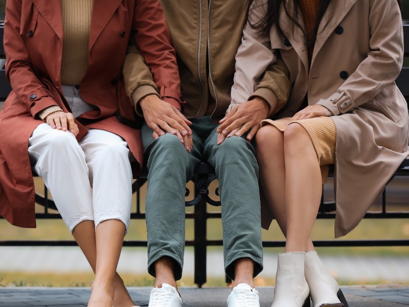 Zwei Frauen und ein Mann auf einer Parkbank, die gegenseitig Händchen halten