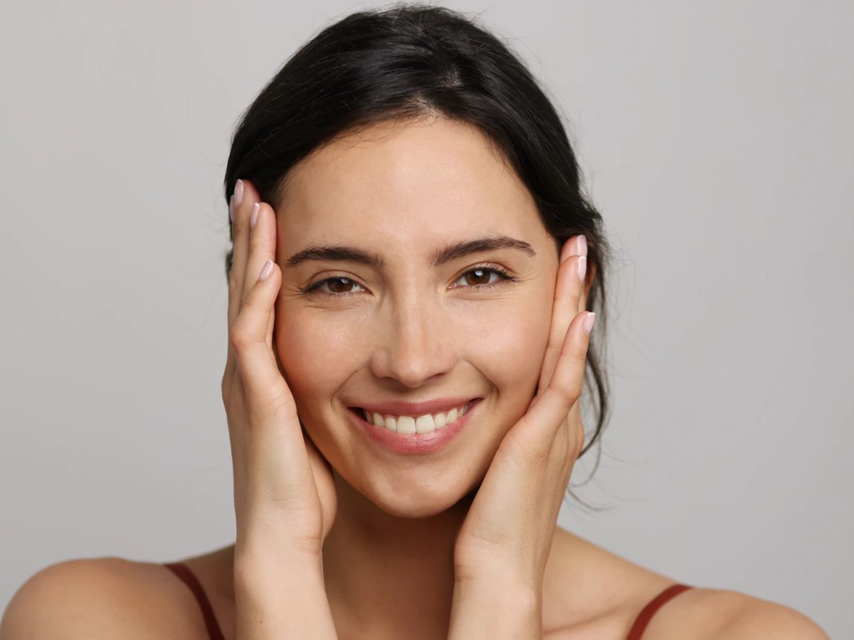 Schöne Frau mit reiner Haut hält sich das Gesicht fest