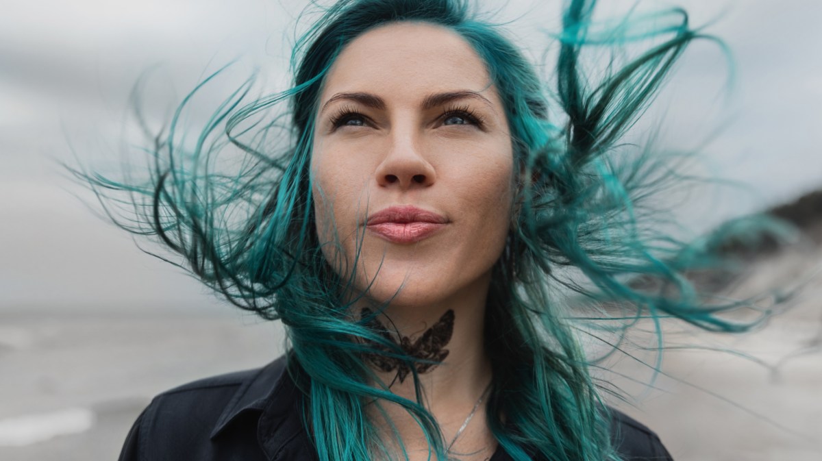 Frau mit blauen Haaren steht am Strand.