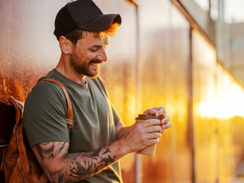 Mann mit Tattoos trinkt To-Go-Kaffee.