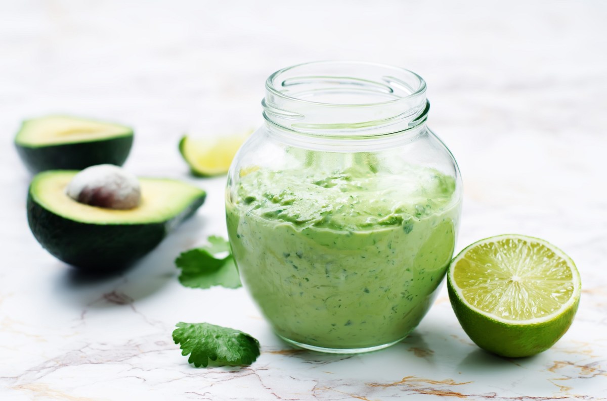 Tzatziki mit Avocado in einem Glas, daneben halbierte Avocados und Limetten.