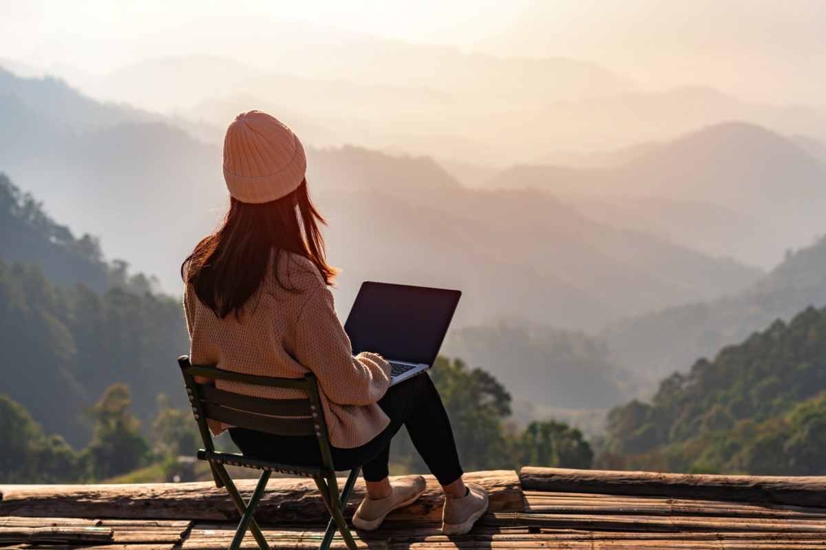 Eine Frau macht einen "Hush Trip" und arbeitet im Wanderurlaub an ihrem Laptop