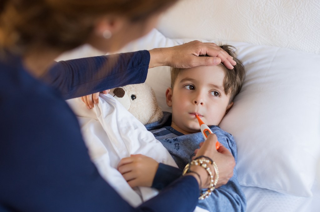 Kranker kleiner Junge liegt im Bett und die Mutter misst Fieber.