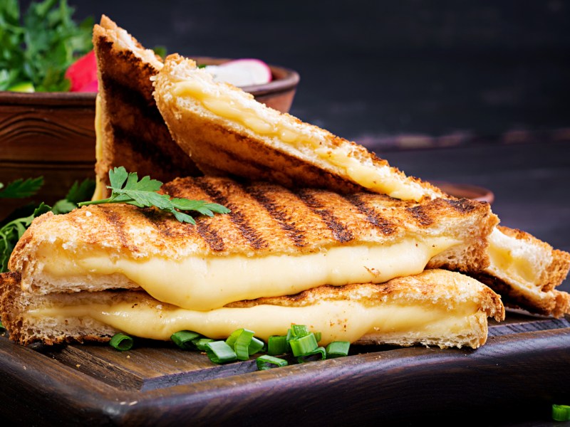 Gegrillte Käsesandwiches auf einem schwarzen Teller. Dazu Salat.