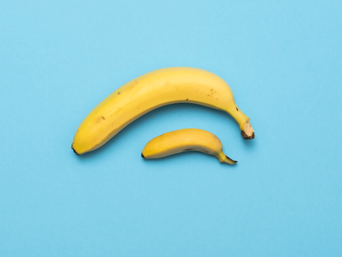 Eine gro&szlig;e und eine kleine gelbe Banane liegen nebeneinander auf einem hellblauen Hintergrund.