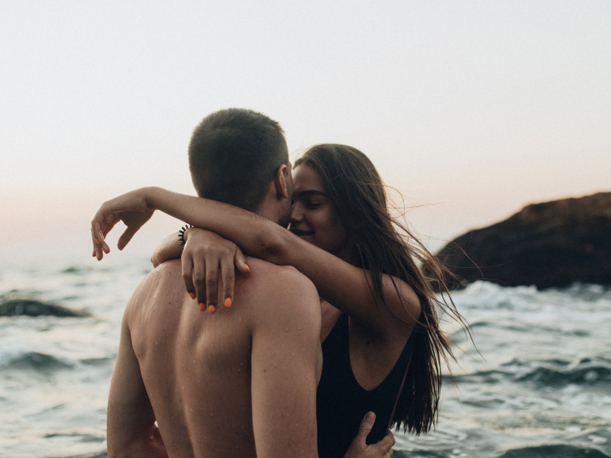 Pärchen am Strand, das sich umarmt, während im Hintergrund die Wellen zu sehen sind