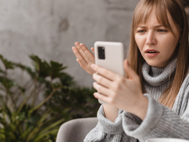 Frau schaut wütend auf ihr Handy.