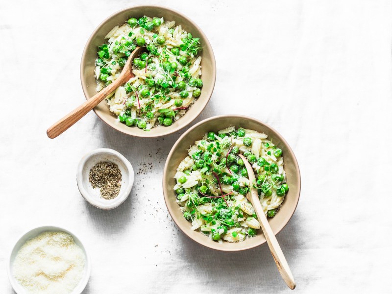 Zwei Teller Orzo-Pasta mit Erbsen und Pesto, darüber Käse und Kresse gestreut, Draufsicht.