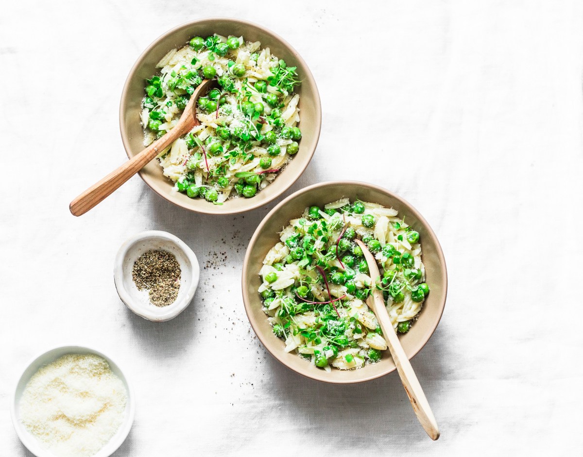 Zwei Teller Orzo-Pasta mit Erbsen und Pesto, darüber Käse und Kresse gestreut, Draufsicht.