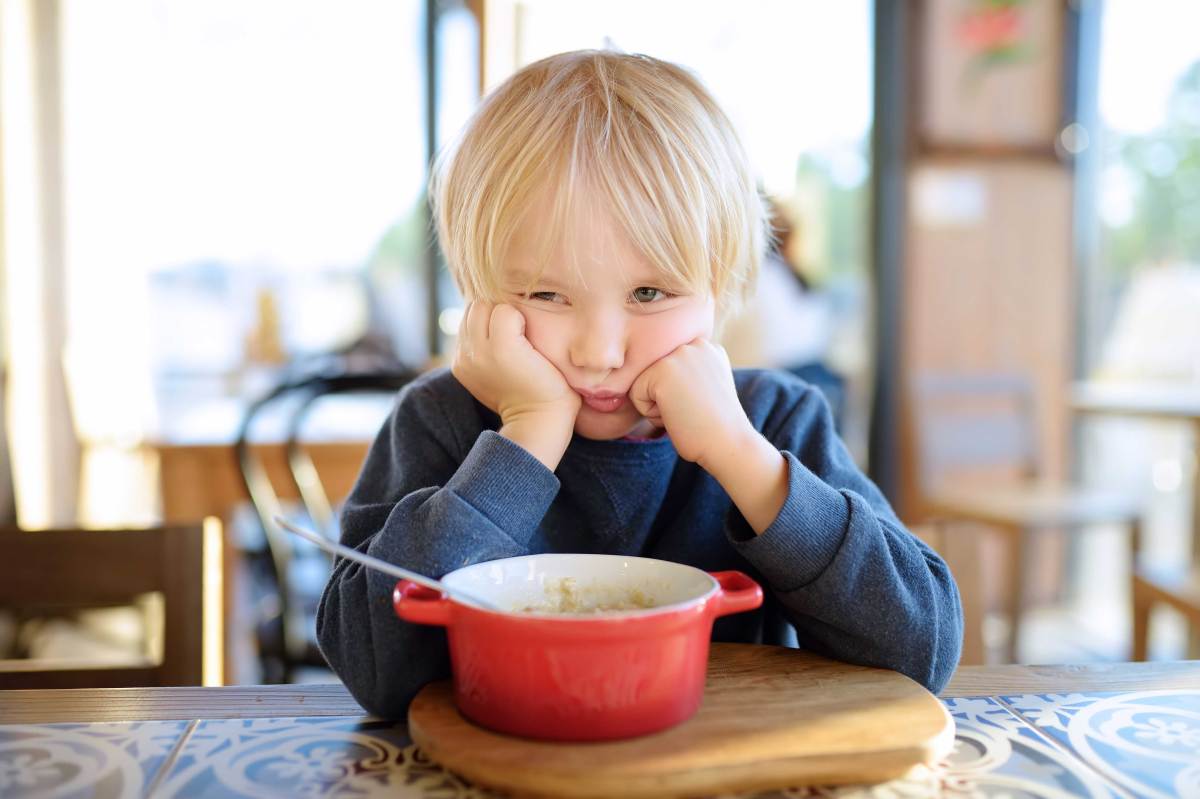 Kind sitzt bockig am Esstisch vor einer Schüssel und weigert sich zu essen.