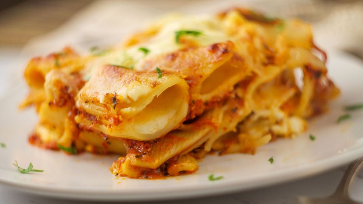 Ziti al forno mit frischen Kräutern auf weißem Pastateller. Frontalansicht.