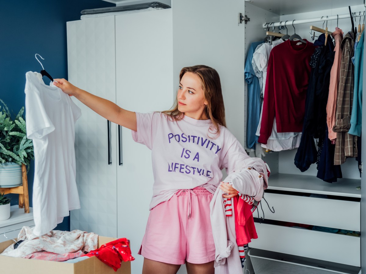 Junge Frau steht vor Kleiderschrank und schaut sich weißes T-Shirt an