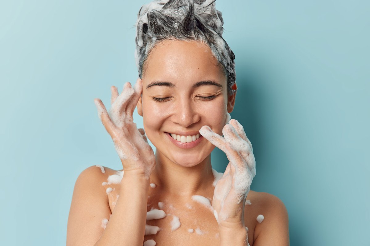 Junge Frau mit eingeschäumten Haaren unter der Dusche.