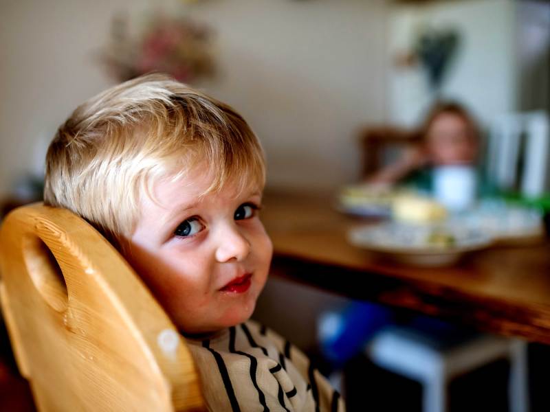 Kleiner Junge sitzt in seinem Hochstuhl am Küchentisch und schaut seitlich in die Kamera.