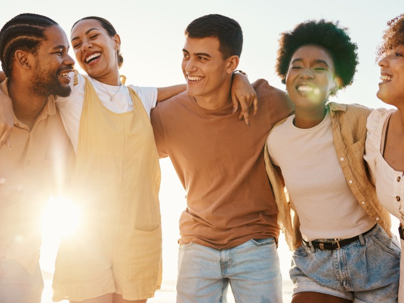 Freunde, die sich zusammen umarmen und lachen, während Sonnenstrahlen durch sie durch scheint